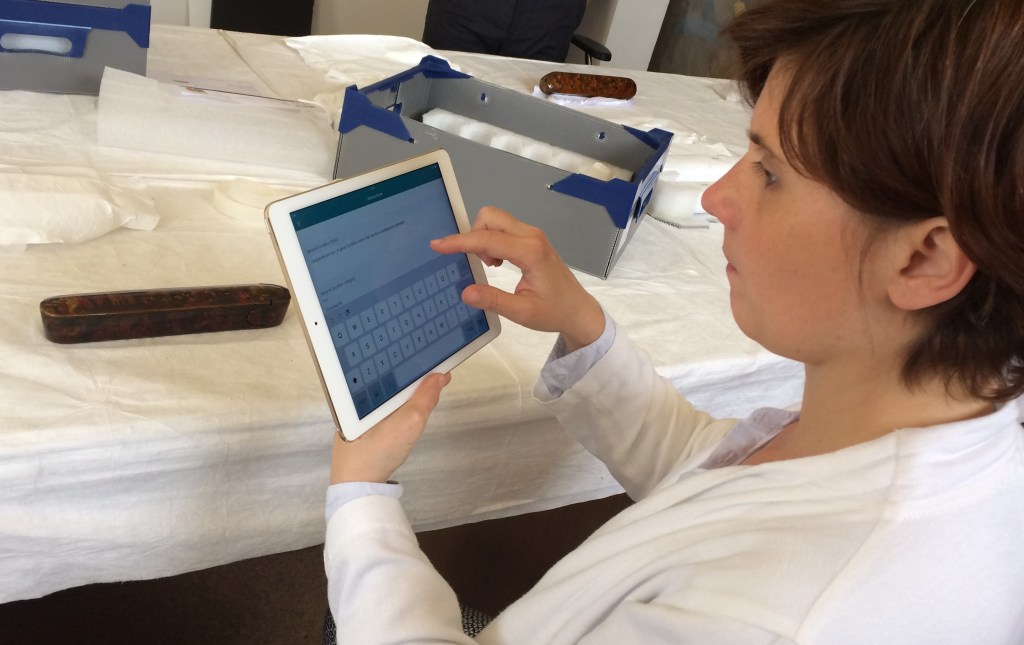 Using an iPad to check the condition of an Iranian lacquered pen box.